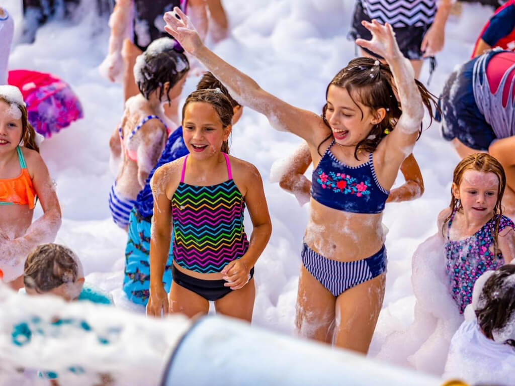 Two young girls laughing and playing in a mountain of soft, white foam at a fun-filled foam party in Franklin Park, PA, enjoying an exciting and safe outdoor experience.