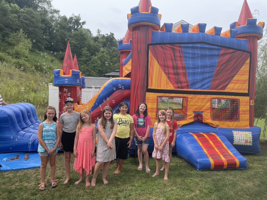 Kids standing in front of colorful inflatable bounce house with slide at backyard party