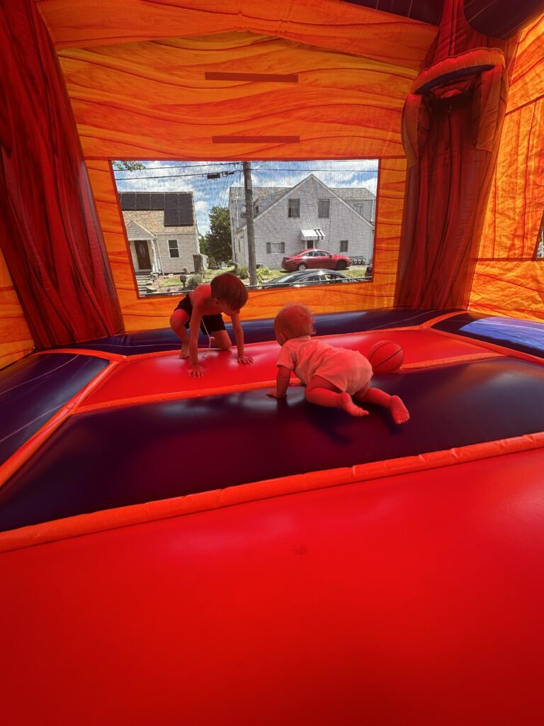 Two children playing inside a red bounce house rental at a backyard party